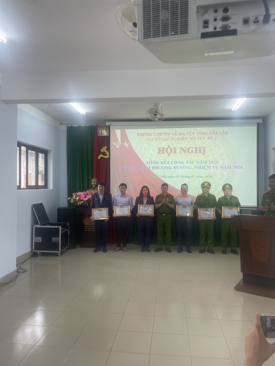 '''A group of people standing in a room with a projector screen
 Description automatically generated'''