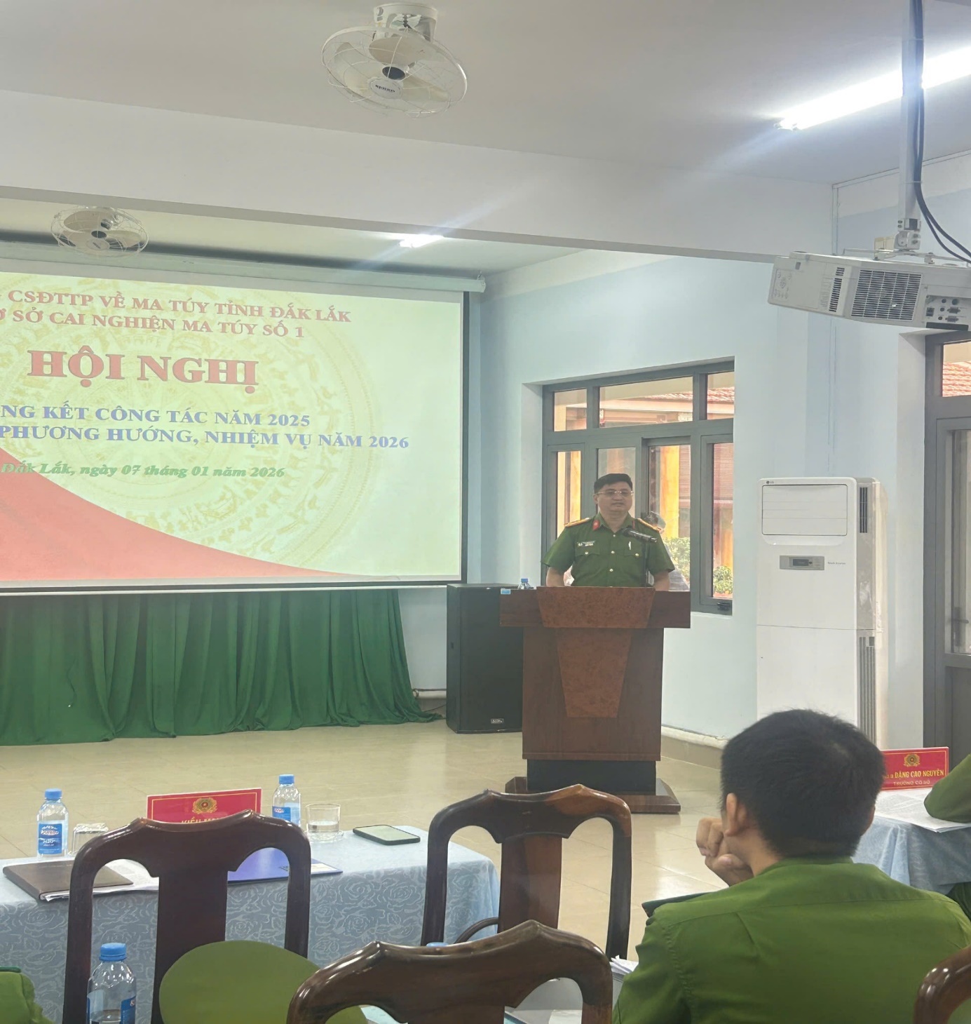 '''A person standing at a podium in front of a projector screen
 Description automatically generated'''